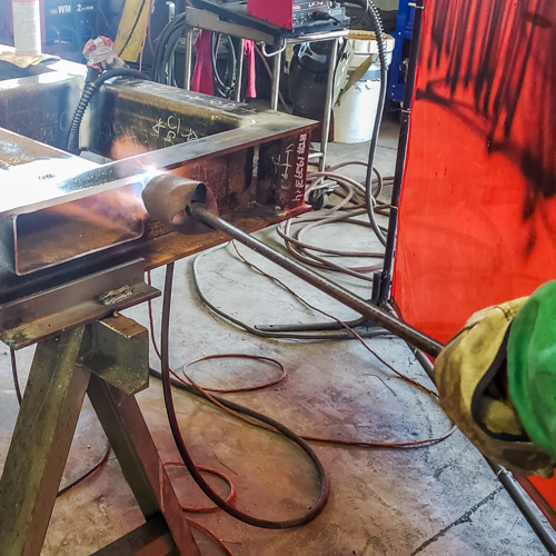 Welder applying heat using the open flame of a blow torch to achieve specified minimum preheat temperature.