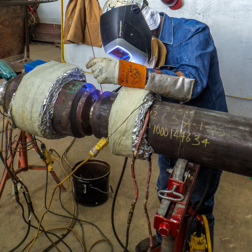 Welder making weld using gas tungsten arc welding (GTAW) on heavy wall pipe for subsea installation. Due to excessive wall thickness, the welder is using resistive blankets, or bead heaters, to achieve and maintain minimum specified preheat temperature.