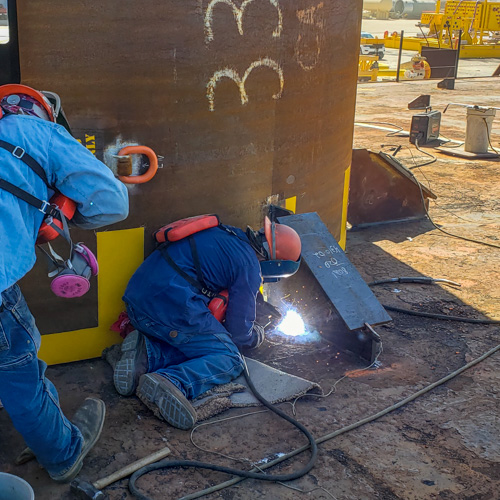 Welder making a sea-fastening weld securing a suction pile, used for installation of subsea manifold, to a barge for deployment in the Gulf of Mexico. This weld was made using flux-core arc welding (FCAW) welding process. This image was captured by the certified welding inspector providing surveillance.